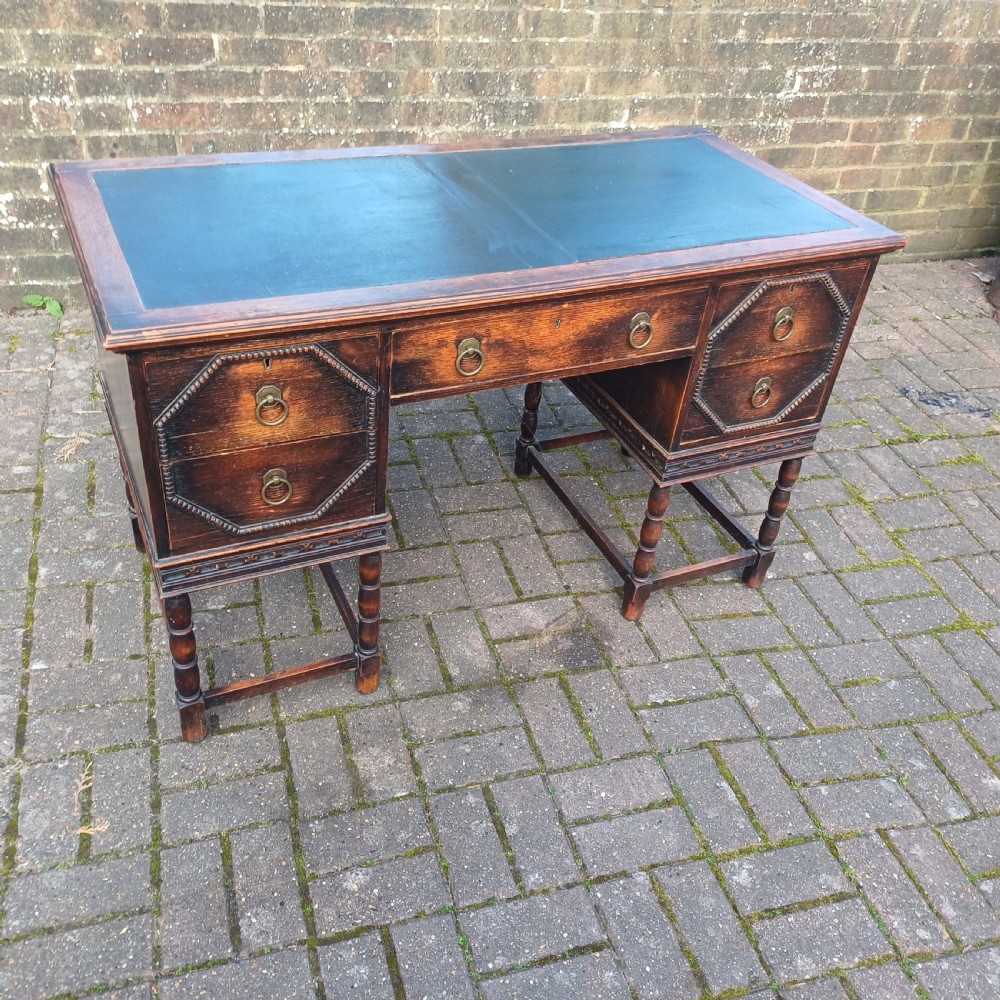 A vintage dark oak writing desk with five drawers, geometric bead moulding, turned legs, brass handles, and a black leather inset top. View II