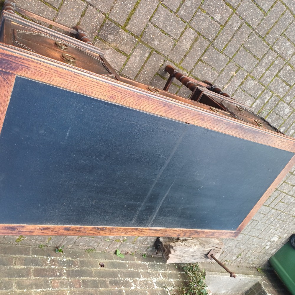A vintage dark oak writing desk with five drawers, geometric bead moulding, turned legs, brass handles, and a black leather inset top. View III