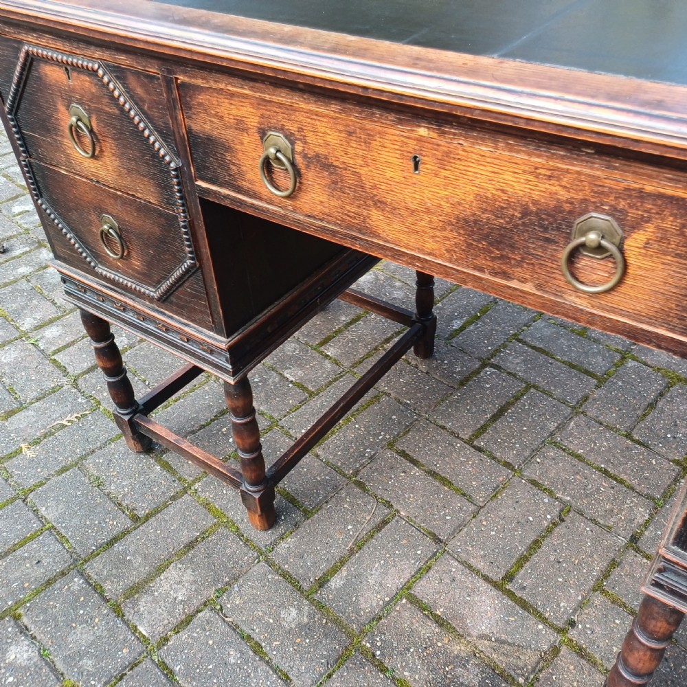 A vintage dark oak writing desk with five drawers, geometric bead moulding, turned legs, brass handles, and a black leather inset top. View VIII