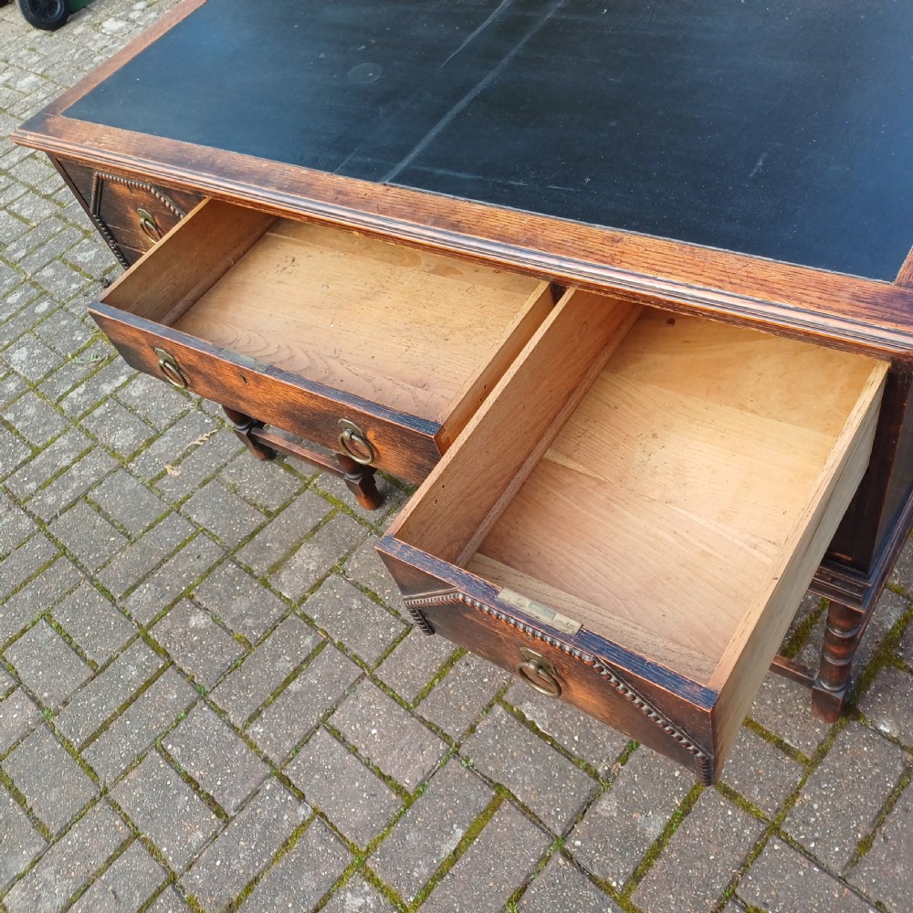 A vintage dark oak writing desk with five drawers, geometric bead moulding, turned legs, brass handles, and a black leather inset top. View IX