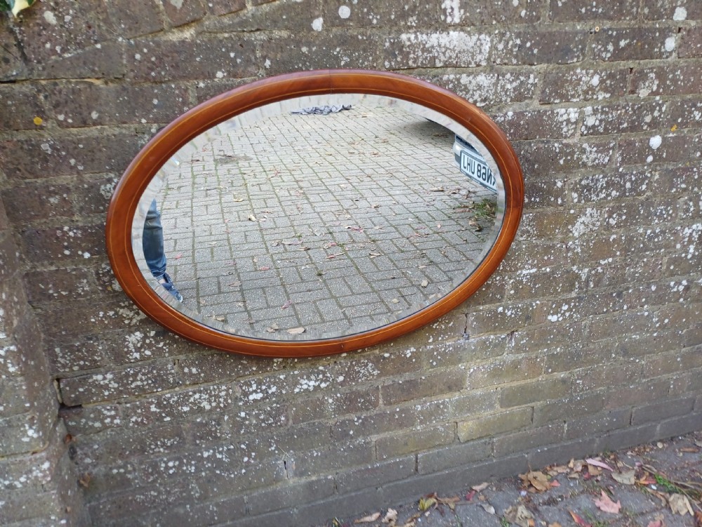 An oval mahogany framed wall mirror featuring a bevelled glass edge and subtle fine string inlay detail around the perimeter. View II