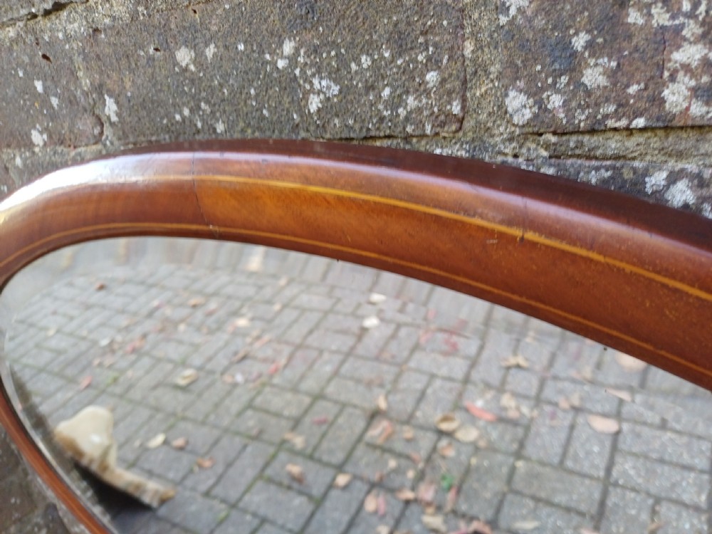 An oval mahogany framed wall mirror featuring a bevelled glass edge and subtle fine string inlay detail around the perimeter. View IV