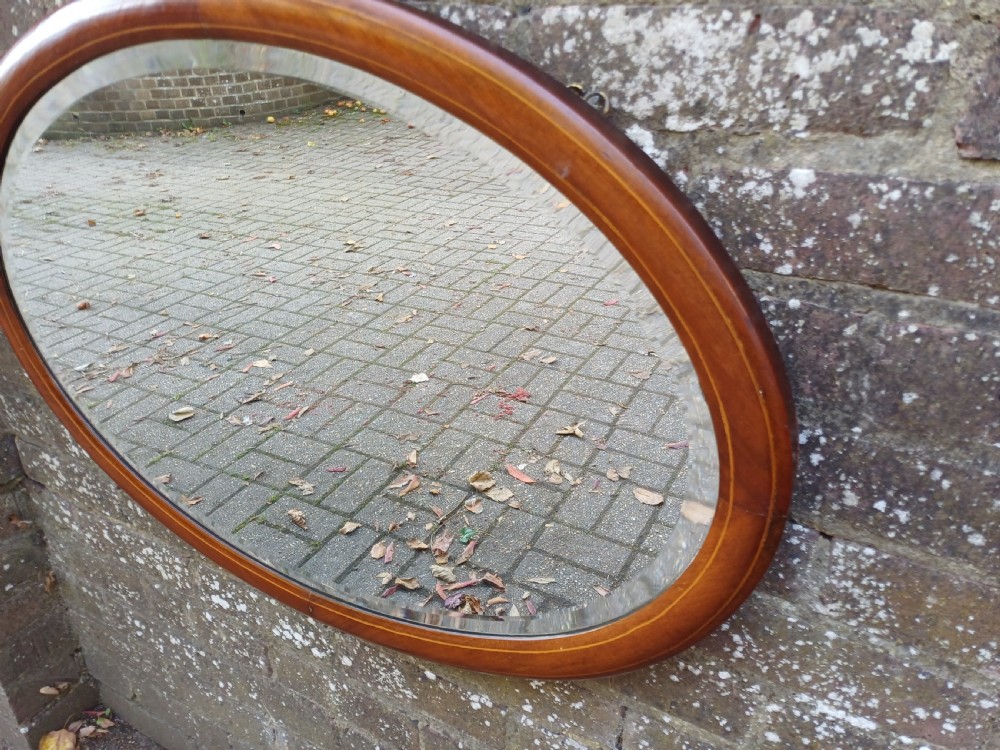 An oval mahogany framed wall mirror featuring a bevelled glass edge and subtle fine string inlay detail around the perimeter. View V