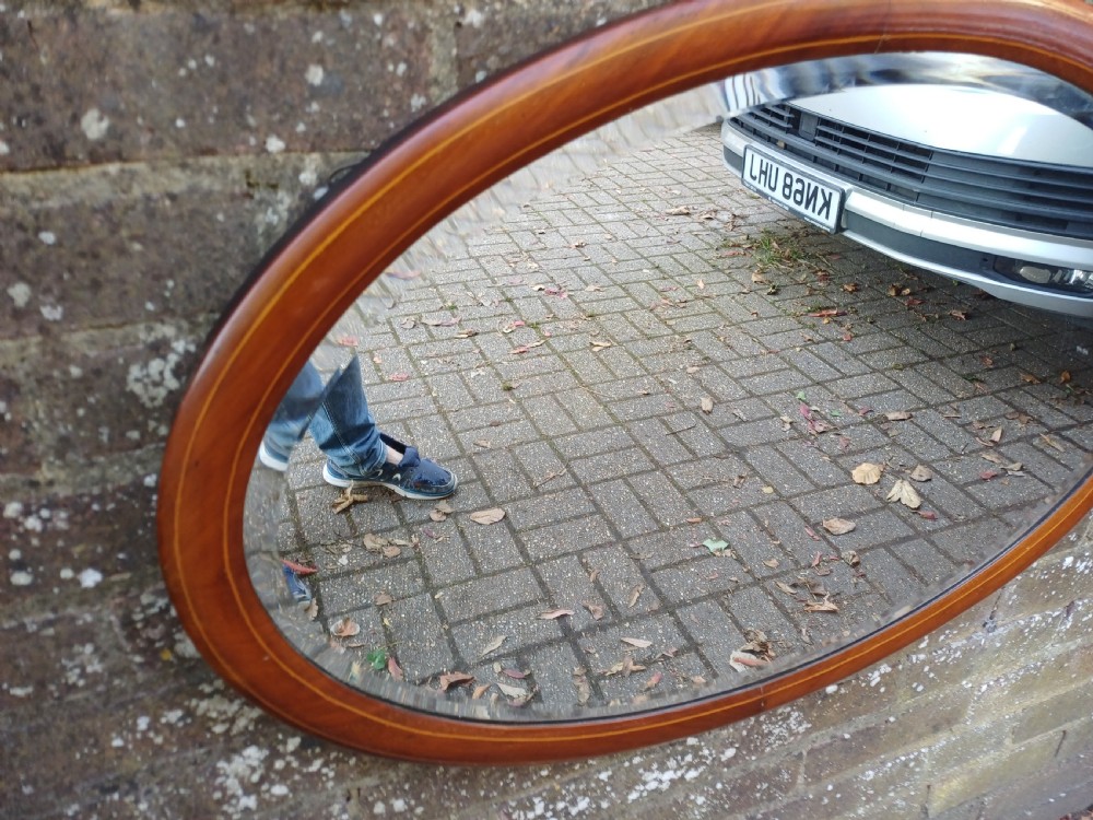 An oval mahogany framed wall mirror featuring a bevelled glass edge and subtle fine string inlay detail around the perimeter. View VI