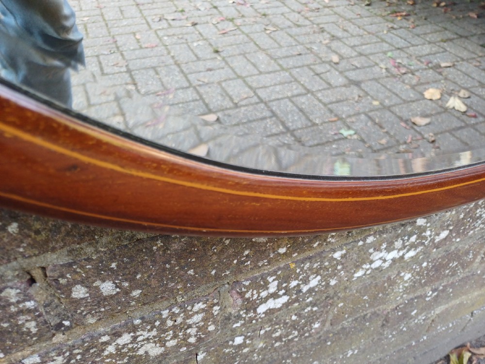 An oval mahogany framed wall mirror featuring a bevelled glass edge and subtle fine string inlay detail around the perimeter. View VII