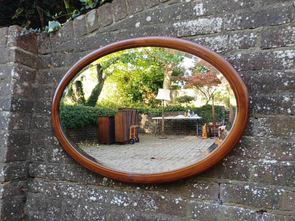 An oval mahogany framed wall mirror featuring a bevelled glass edge and subtle fine string inlay detail around the perimeter. View IX