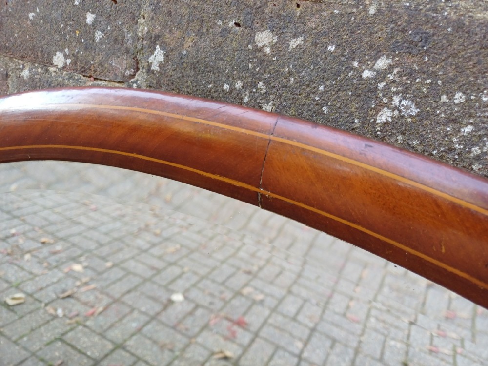 An oval mahogany framed wall mirror featuring a bevelled glass edge and subtle fine string inlay detail around the perimeter. View X