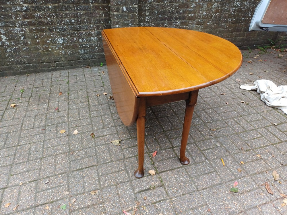An antique mahogany drop-leaf dining table with one hinged leaf raised, standing on tapered legs with pad feet.
