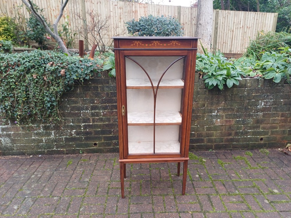An Edwardian mahogany display cabinet featuring a glazed single door with curved glazing bars, satinwood marquetry inlay, fabric-lined shelves, and tapered square legs.