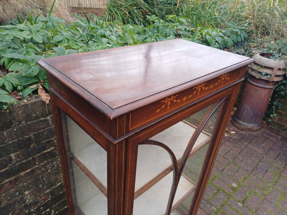 An Edwardian mahogany display cabinet featuring a glazed single door with curved glazing bars, satinwood marquetry inlay, fabric-lined shelves, and tapered square legs. View II