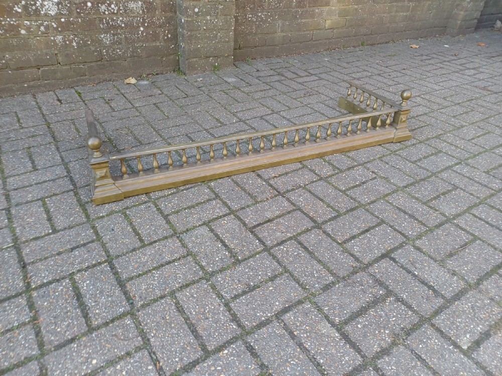 An antique brass fireplace fender featuring a turned spindle balustrade, spherical corner finials, and a stepped plinth base. View II