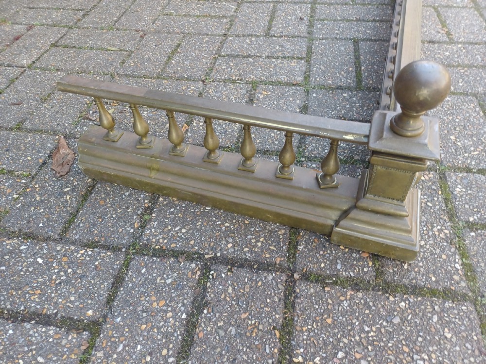 An antique brass fireplace fender featuring a turned spindle balustrade, spherical corner finials, and a stepped plinth base. View V