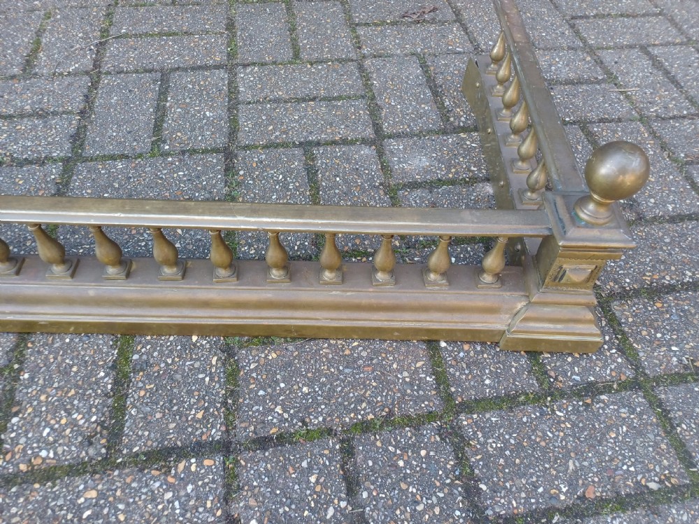An antique brass fireplace fender featuring a turned spindle balustrade, spherical corner finials, and a stepped plinth base. View VII