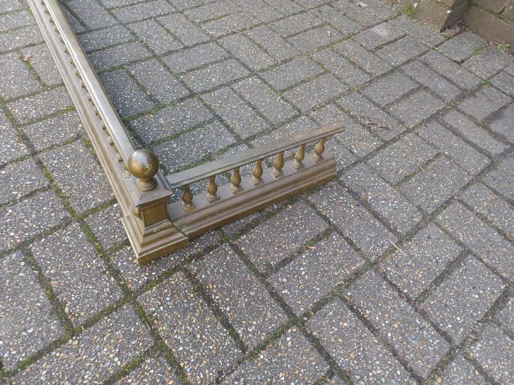 An antique brass fireplace fender featuring a turned spindle balustrade, spherical corner finials, and a stepped plinth base. View IX