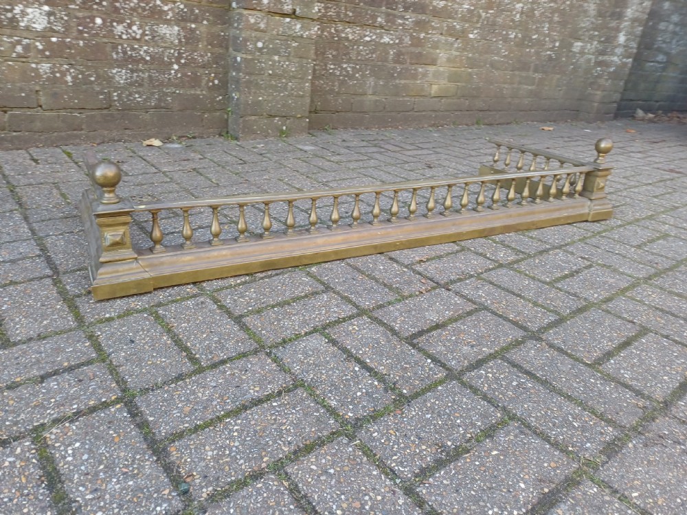 An antique brass fireplace fender featuring a turned spindle balustrade, spherical corner finials, and a stepped plinth base. View XII