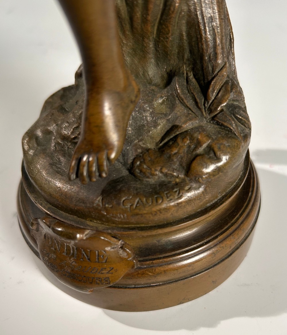 A patinated bronze sculpture of a winged female figure standing on a circular moulded base with an inscribed title plaque. View III