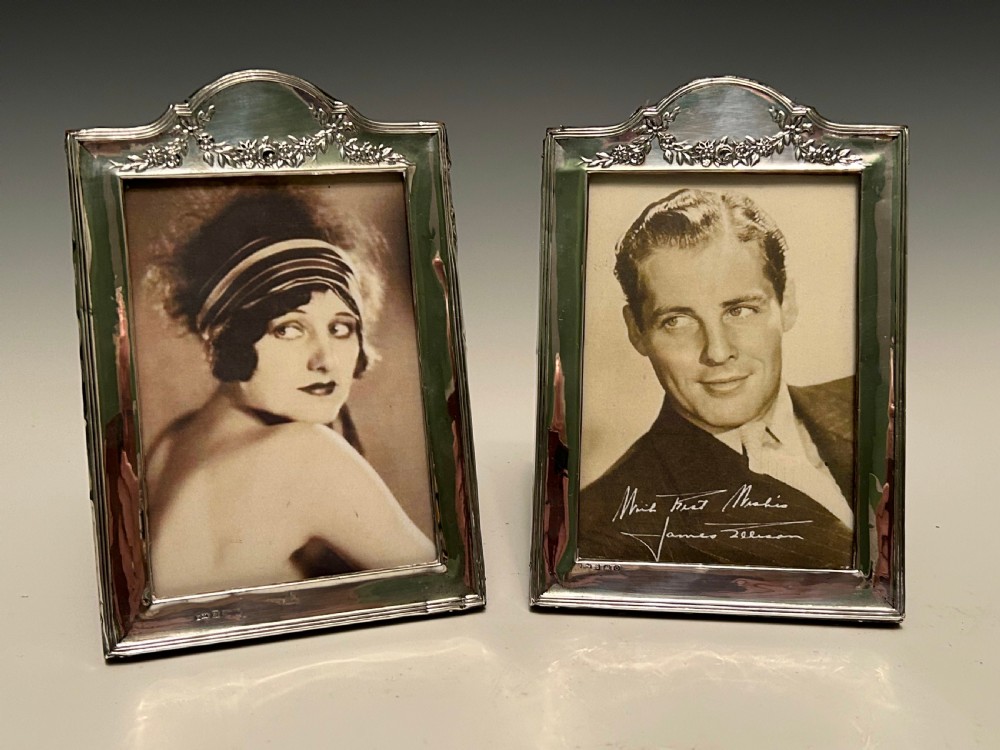 A pair of Edwardian hallmarked sterling silver picture frames with arched tops and floral relief moulding housing vintage black and white portrait photographs.