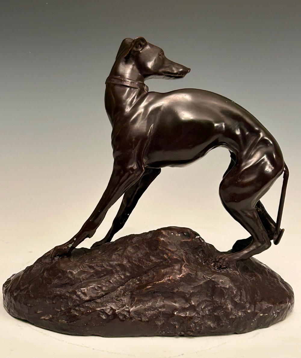 A dark brown patinated bronze sculpture depicting an alert standing greyhound on a textured naturalistic base. View II