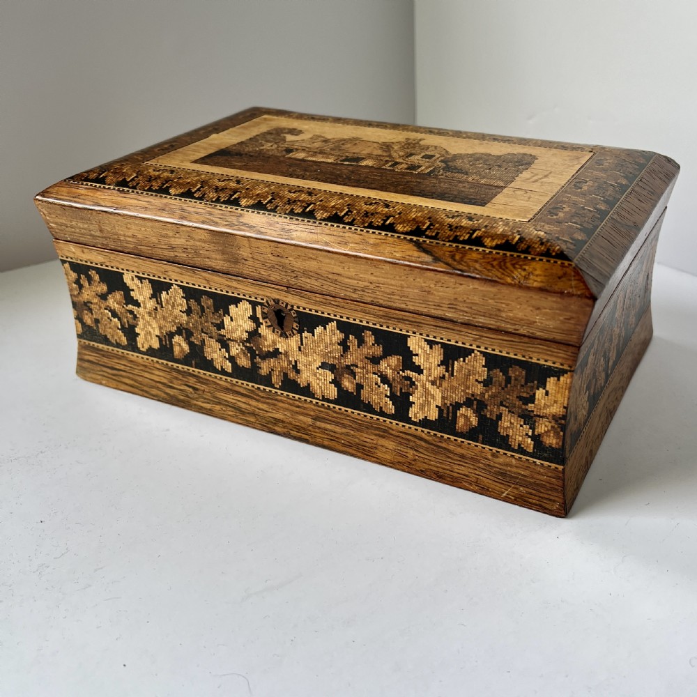 A rectangular Victorian Tunbridge ware wooden box featuring flared concave sides, a hinged lid decorated with an inlaid landscape, and leaf mosaic borders.