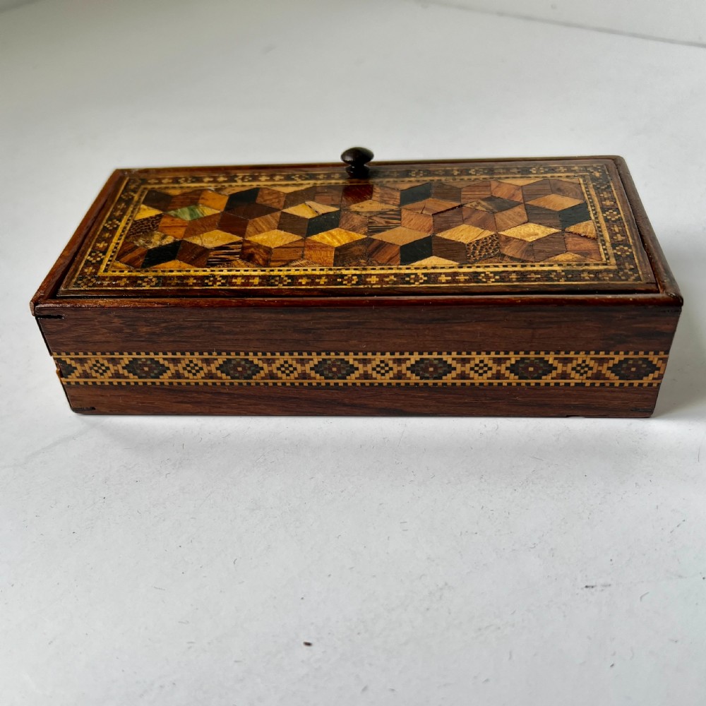 A small rectangular wooden trinket box featuring a geometric tumbling block mosaic lid and an inlaid patterned border.