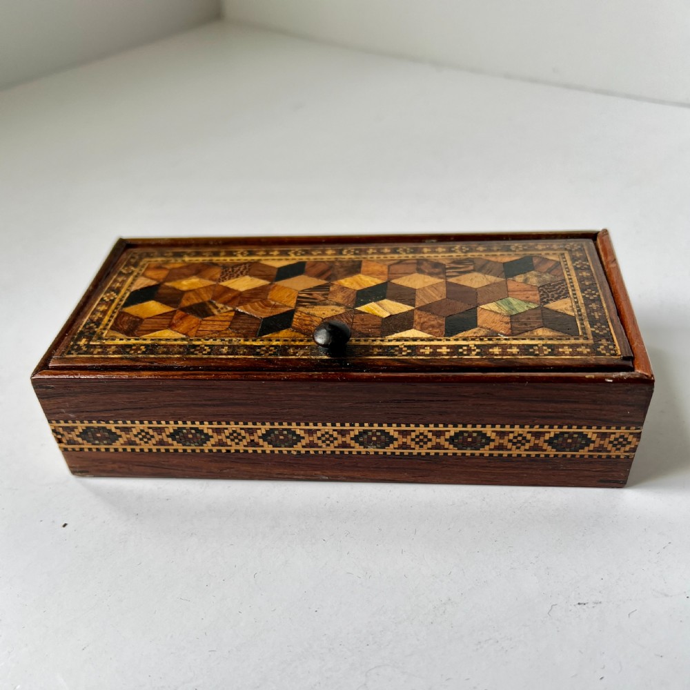 A small rectangular wooden trinket box featuring a geometric tumbling block mosaic lid and an inlaid patterned border. View V