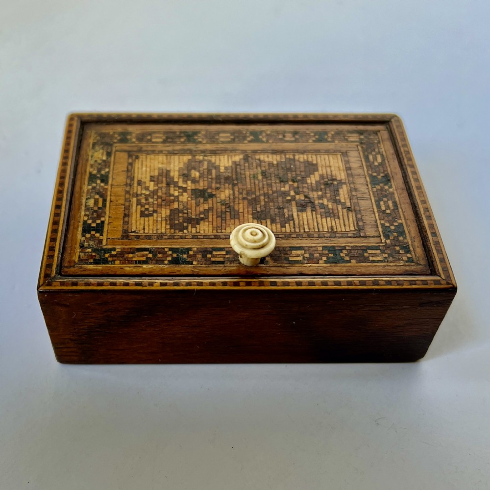 A small rectangular Victorian Tunbridge ware box made from polished dark wood, featuring a tessellated geometric border, central floral wood mosaic lid, and a small carved bone knob.