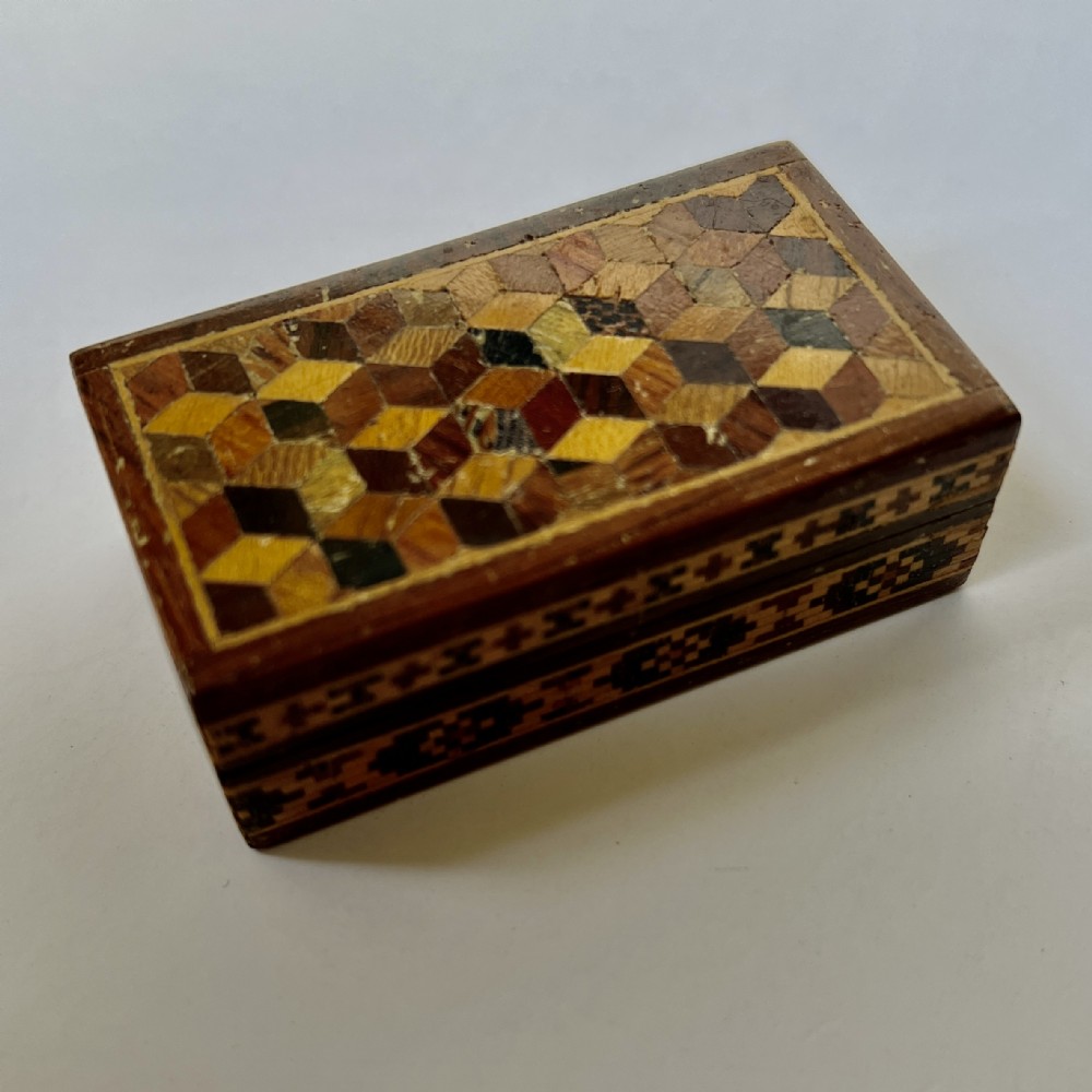 A small rectangular wooden box featuring a geometric tumbling block parquetry lid and a mosaic pattern band around the sides.