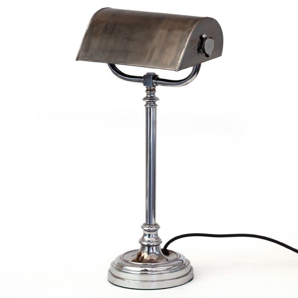 An Art Deco style chrome desk lamp featuring a curved trough-shaped metal shade mounted on a slender stem and stepped base.