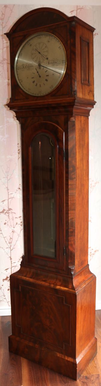 fig 2. A Regency flame mahogany astronomical regulator longcase clock featuring an arched hood, silvered dial with three sub-dials, glass trunk door, and plinth base.