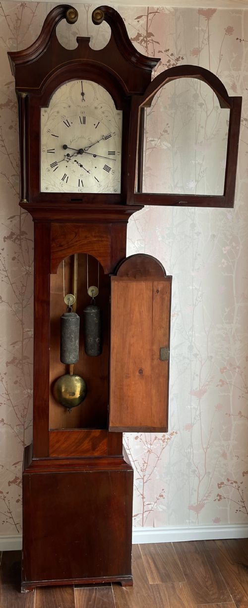 fig 1. A Georgian Scottish mahogany longcase clock featuring a swan-neck pediment, an arched dial with Roman numerals, and a flame mahogany trunk door.