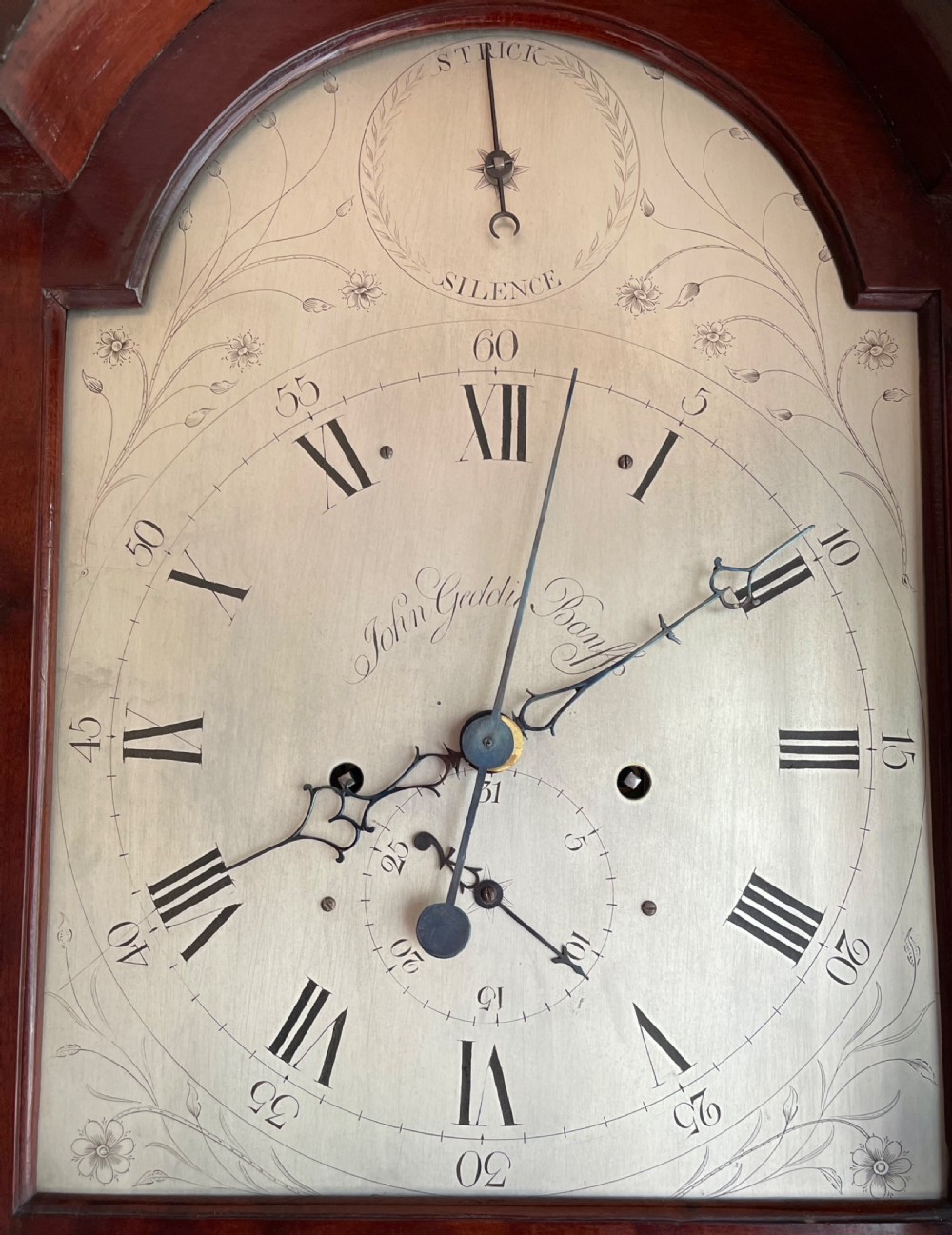 A Georgian Scottish mahogany longcase clock featuring a swan-neck pediment, an arched dial with Roman numerals, and a flame mahogany trunk door. View V