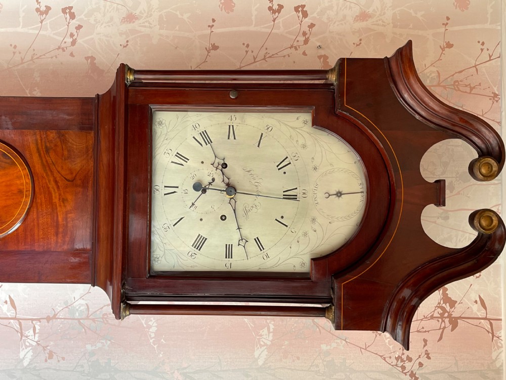 A Georgian Scottish mahogany longcase clock featuring a swan-neck pediment, an arched dial with Roman numerals, and a flame mahogany trunk door. View VI