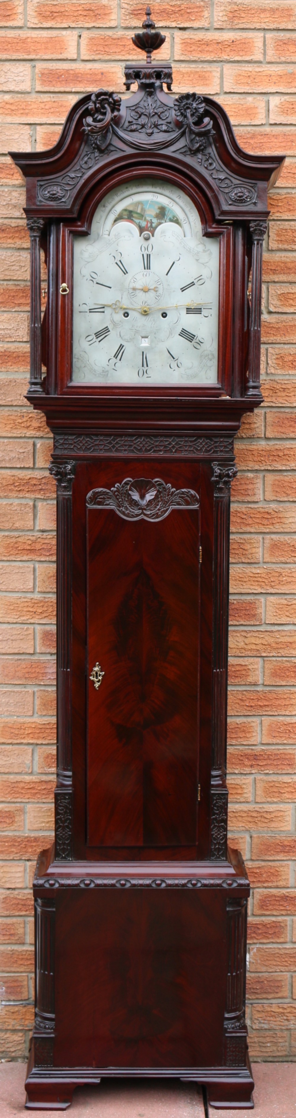 An 18th-century Chippendale flame mahogany longcase clock featuring a swan-neck pediment, reeded columns, and a painted arch dial face.