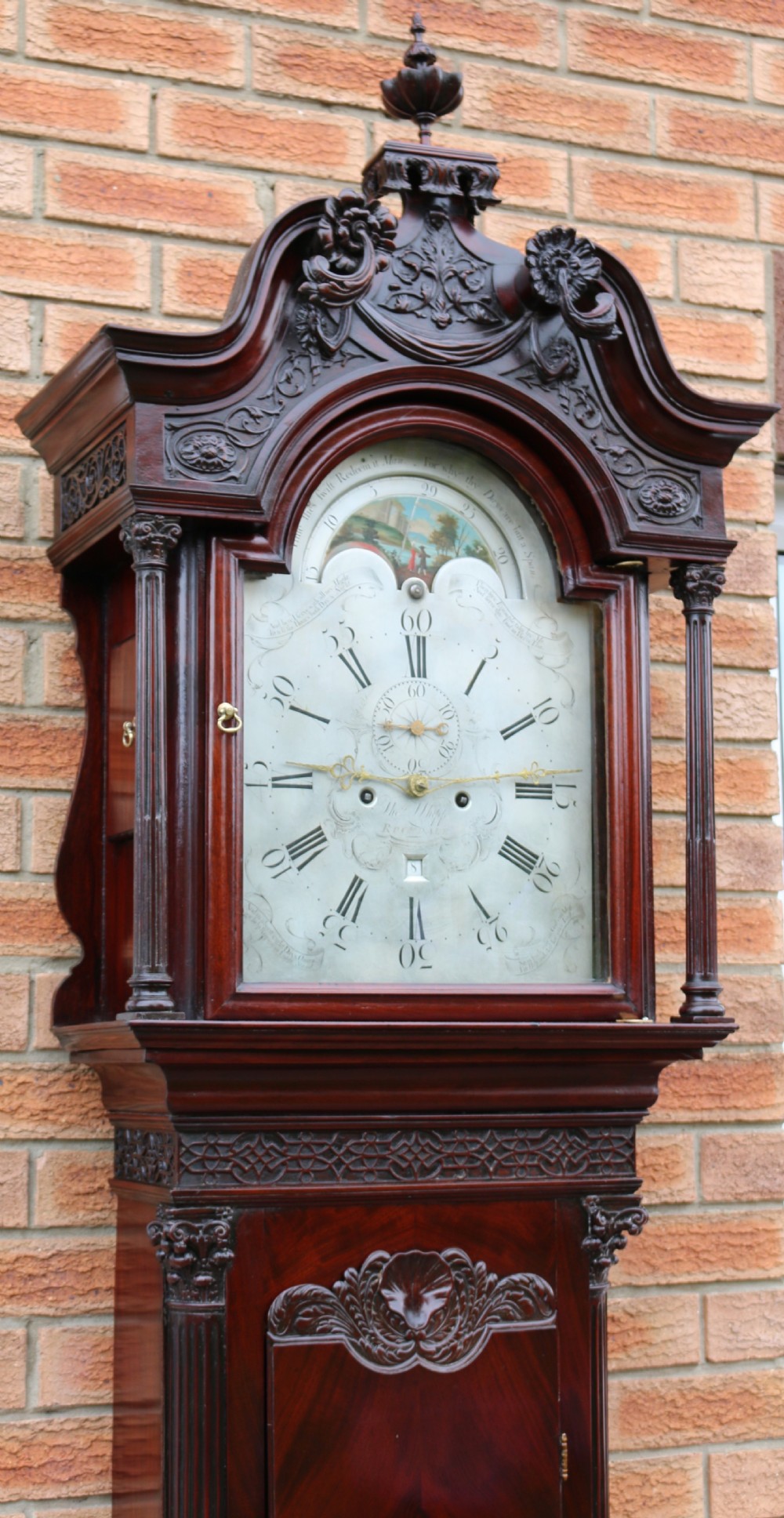 An 18th-century Chippendale flame mahogany longcase clock featuring a swan-neck pediment, reeded columns, and a painted arch dial face. View V
