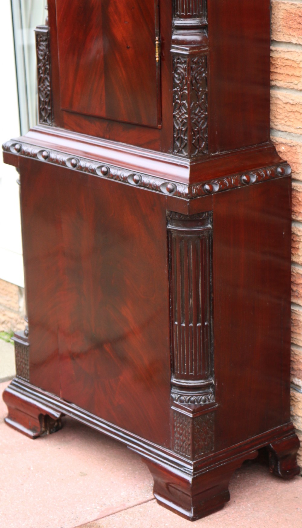 An 18th-century Chippendale flame mahogany longcase clock featuring a swan-neck pediment, reeded columns, and a painted arch dial face. View VI