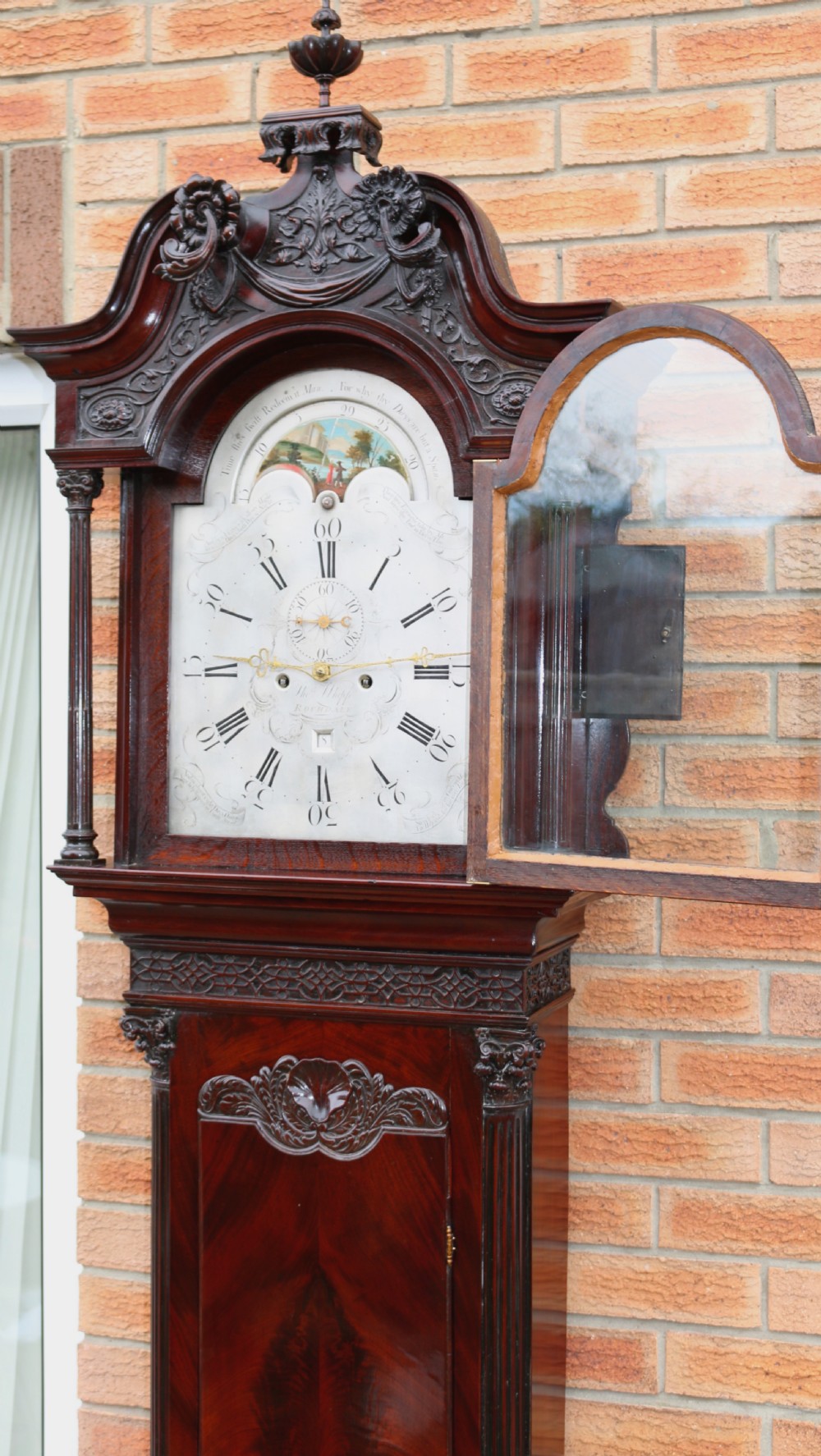 An 18th-century Chippendale flame mahogany longcase clock featuring a swan-neck pediment, reeded columns, and a painted arch dial face. View XII