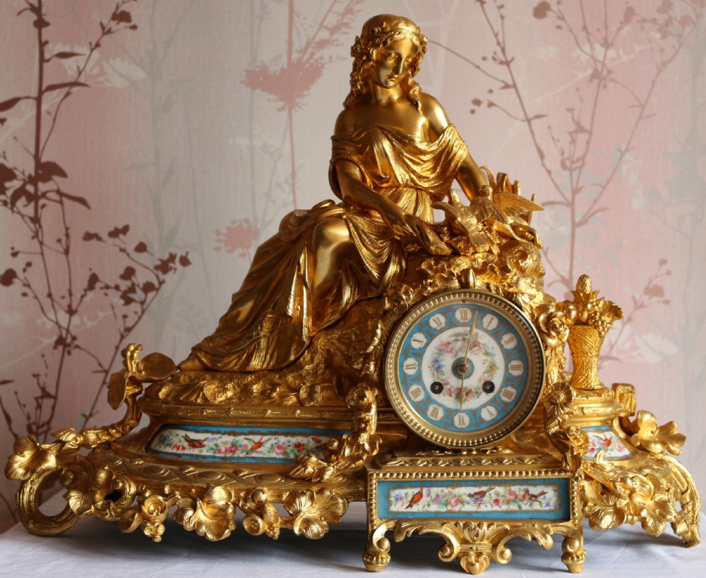An ornate 19th-century French gilt bronze ormolu mantel clock topped with a classic draped female figure, featuring turquoise porcelain panels painted with flowers and birds.