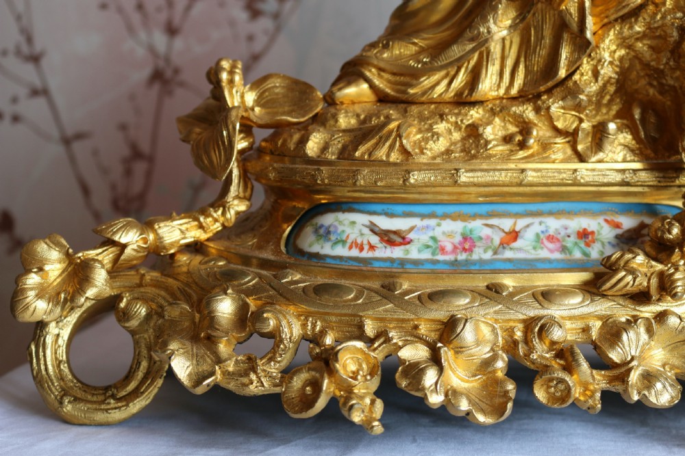 An ornate 19th-century French gilt bronze ormolu mantel clock topped with a classic draped female figure, featuring turquoise porcelain panels painted with flowers and birds. View XIV