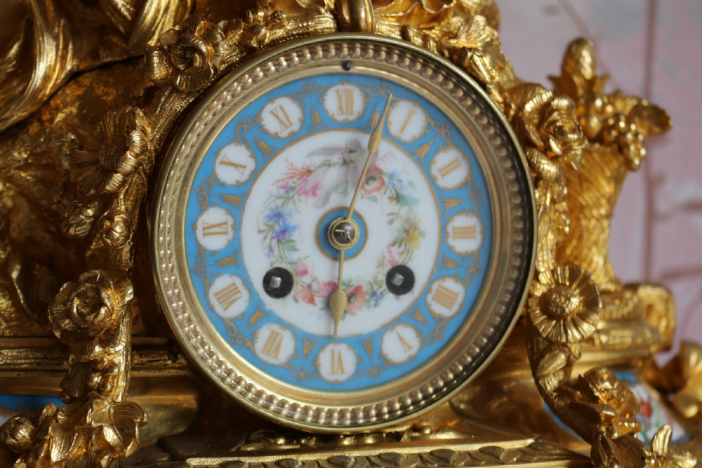 An ornate 19th-century French gilt bronze ormolu mantel clock topped with a classic draped female figure, featuring turquoise porcelain panels painted with flowers and birds. View XVI