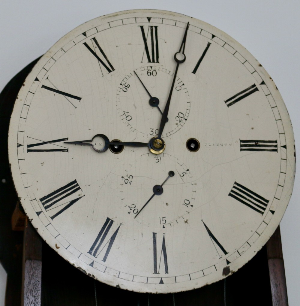 A tall flame mahogany Scottish regulator longcase clock featuring a circular white painted dial, carved top scrollwork, and a glazed door showing brass weights. View VIII