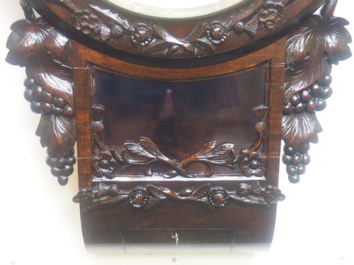 fig 2. An antique Victorian carved dark mahogany wall clock featuring an off-white dial with Roman numerals marked Berry Cardiff, framed by thistle and vine carvings.