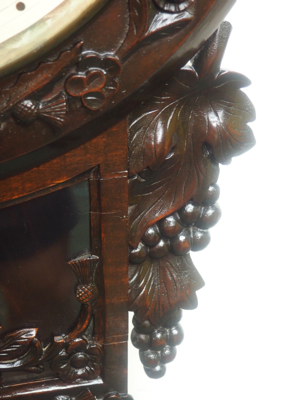 An antique Victorian carved dark mahogany wall clock featuring an off-white dial with Roman numerals marked Berry Cardiff, framed by thistle and vine carvings. View V