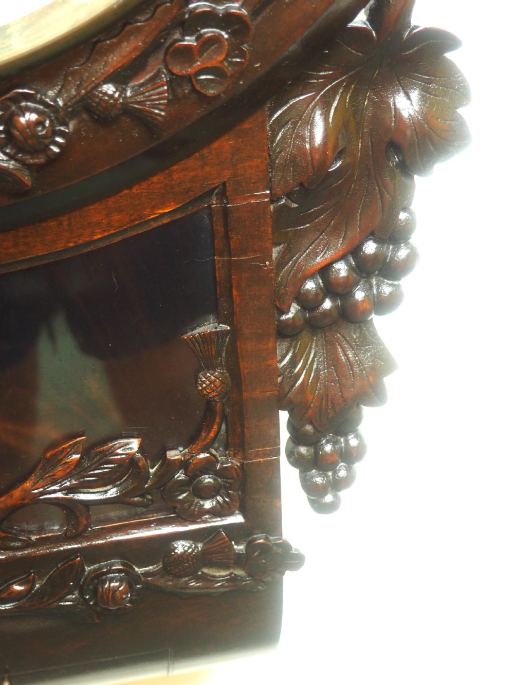 An antique Victorian carved dark mahogany wall clock featuring an off-white dial with Roman numerals marked Berry Cardiff, framed by thistle and vine carvings. View VI