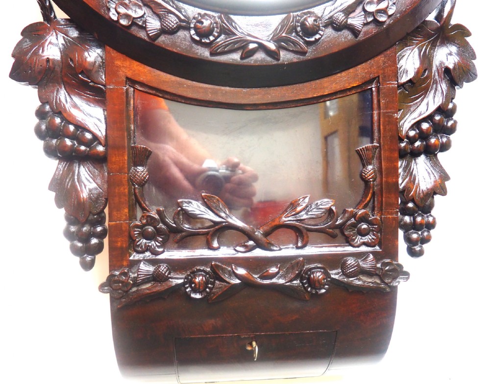 An antique Victorian carved dark mahogany wall clock featuring an off-white dial with Roman numerals marked Berry Cardiff, framed by thistle and vine carvings. View XII