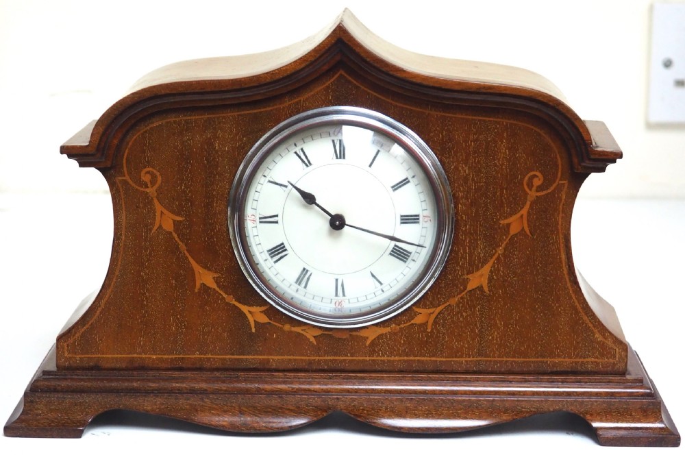 An Edwardian mahogany mantel clock featuring a stepped tulip-top case, floral marquetry inlay, and a white circular dial with Roman numerals.