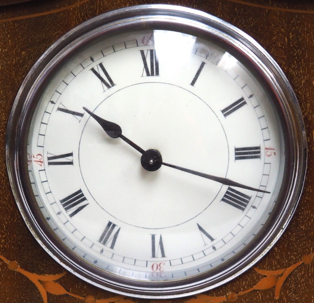 An Edwardian mahogany mantel clock featuring a stepped tulip-top case, floral marquetry inlay, and a white circular dial with Roman numerals. View IV