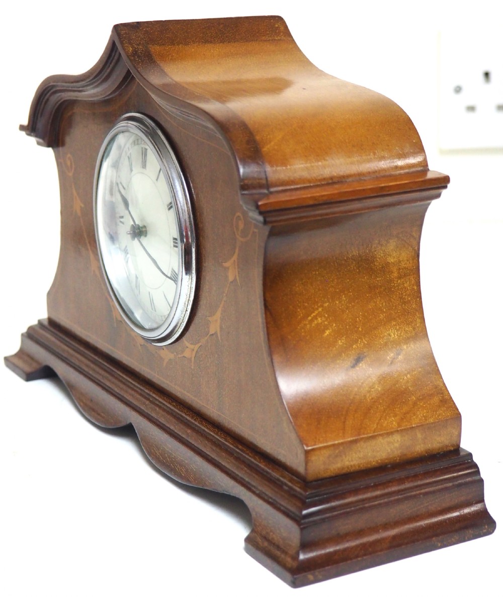 An Edwardian mahogany mantel clock featuring a stepped tulip-top case, floral marquetry inlay, and a white circular dial with Roman numerals. View VII