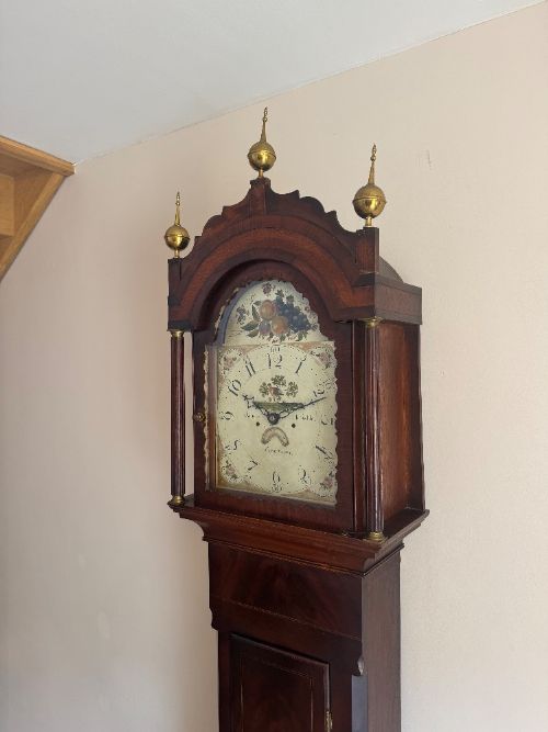 fig 1. An 18th-century mahogany longcase clock featuring a hand-painted dial with botanical details, brass urn finials, and an arched hood.