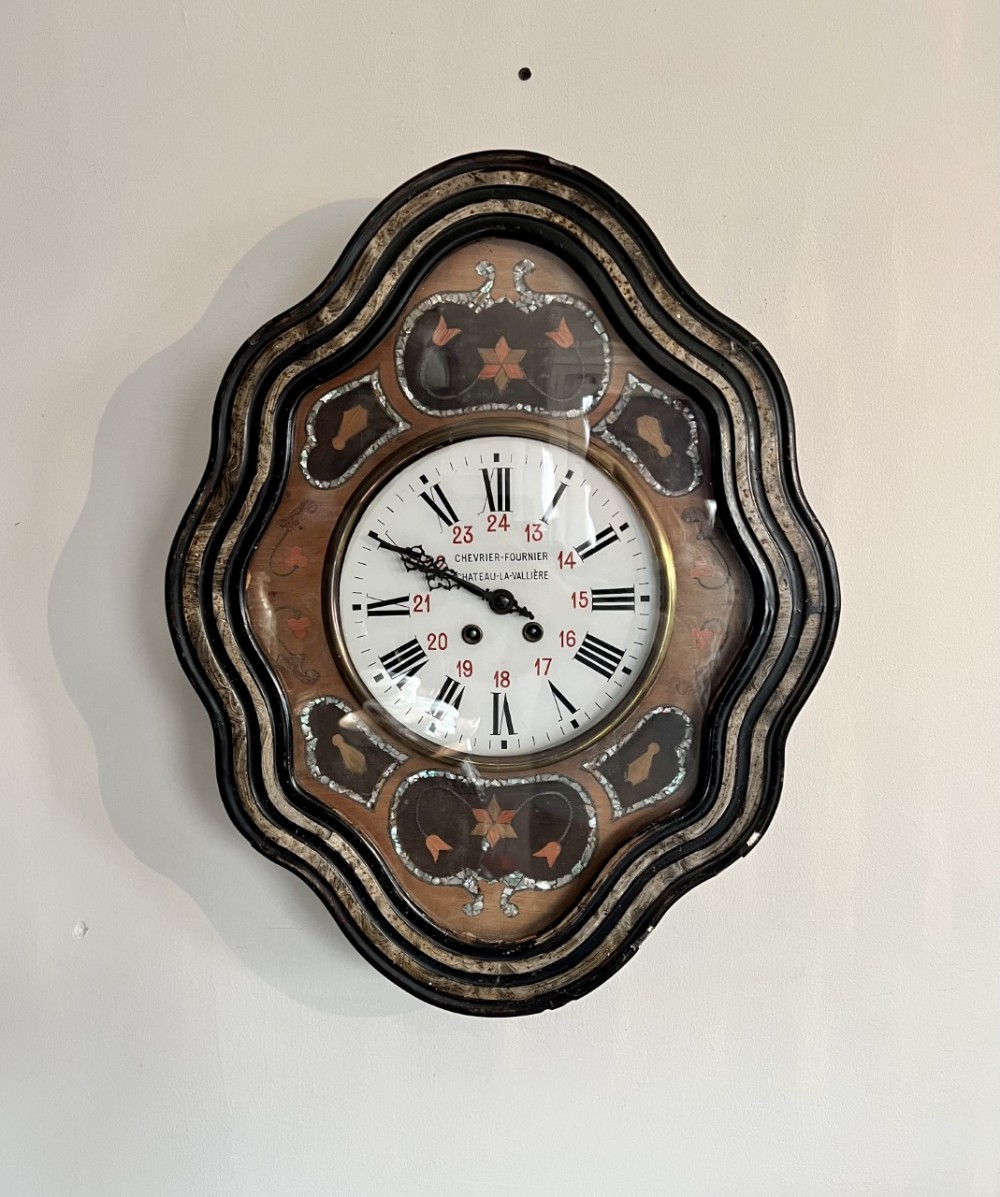 An antique French wall clock with a scalloped ebonised wood frame, mother-of-pearl inlay, and a white enamel dial with Roman numerals.