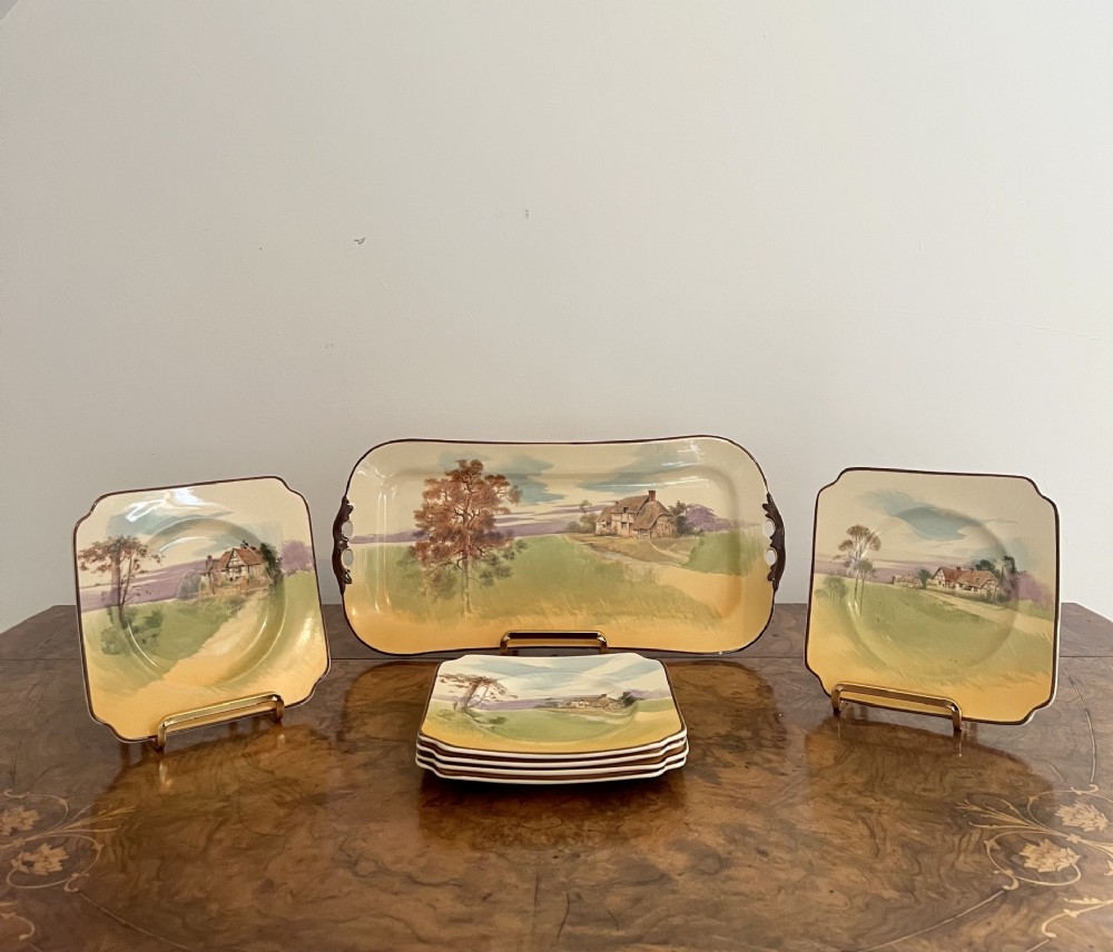 A set of seven Royal Doulton ceramic pieces, including one large rectangular tray and six square plates with cottage landscape paintings.
